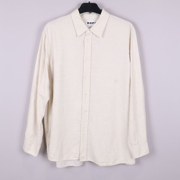 Beige skjorta med långa ärmar och krage hängande på galge