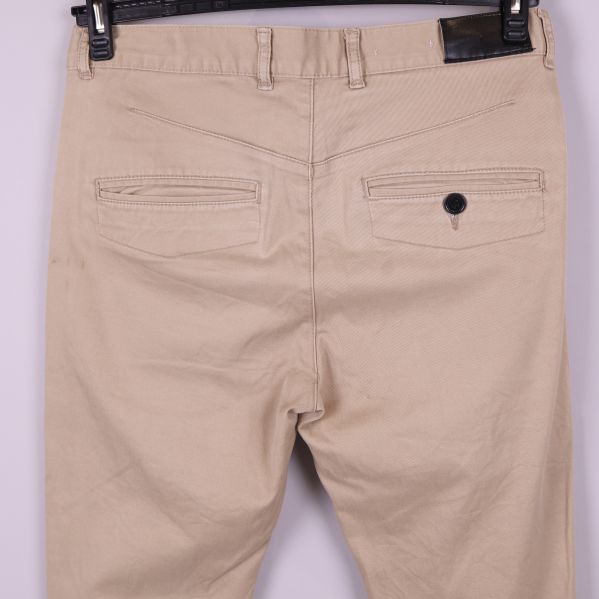 Närbild bakfickor på beiga chinos med knapp