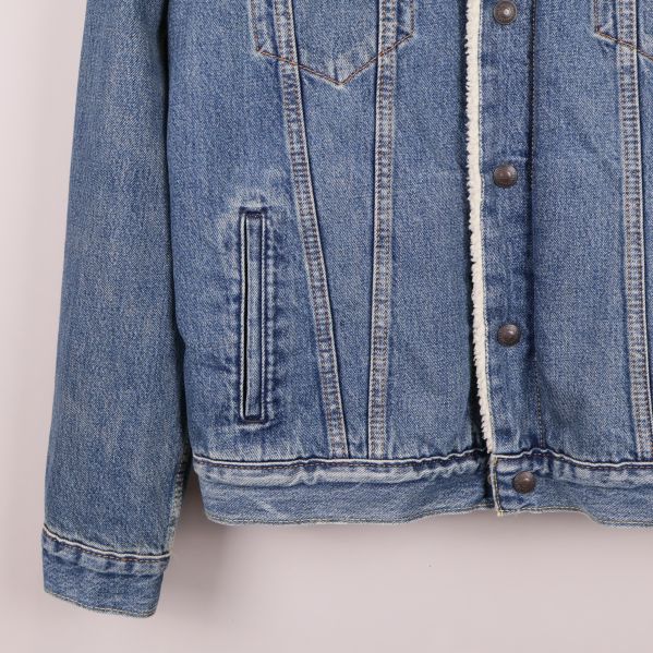 Nedre vänstra del av jeansjacka, ficka och fåll i fokus