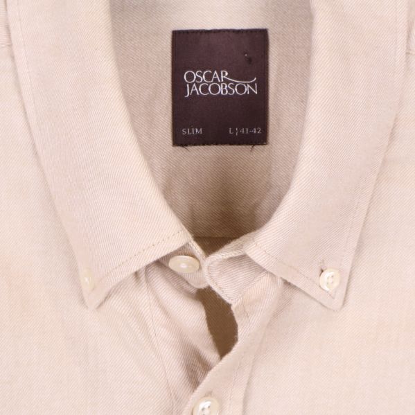 Närbild på beige skjortas krage och Oscar Jacobson-etikett