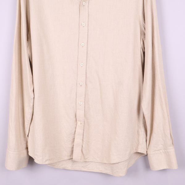 Nedre delen av beige skjorta med knappslå och rundad fåll