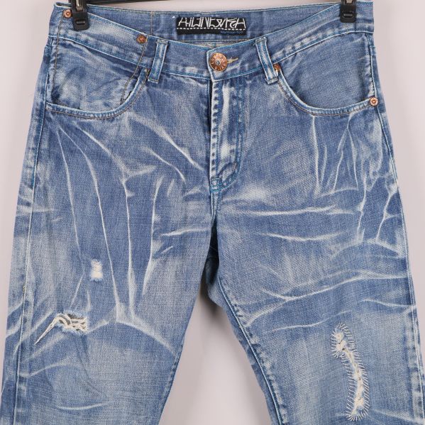 Närbild på slitna detaljer på låren framtill på jeansen