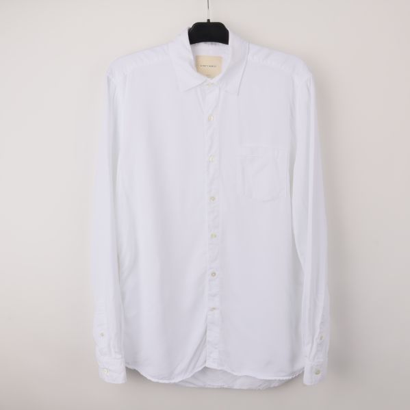 Vit långärmad skjorta på galge mot ljus bakgrund