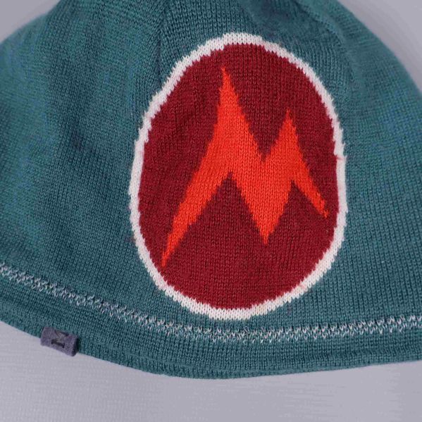 Närbild på grafiskt märke i rött och orange på mössan