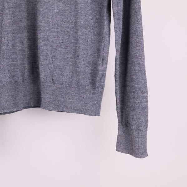 Närbild på nederkant och ärm av grå stickad tröja