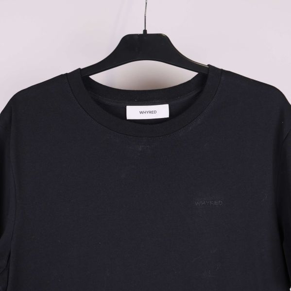 Närbild upptill på svart t-shirt med diskret ton-i-ton logga