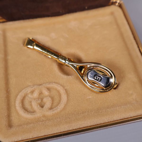 Närbild på guldfärgad slipsklämma med silvrig GG-detalj