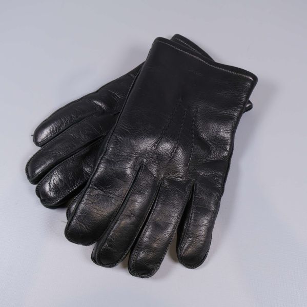 Ett par svarta skinnhandskar liggande mot ljus bakgrund