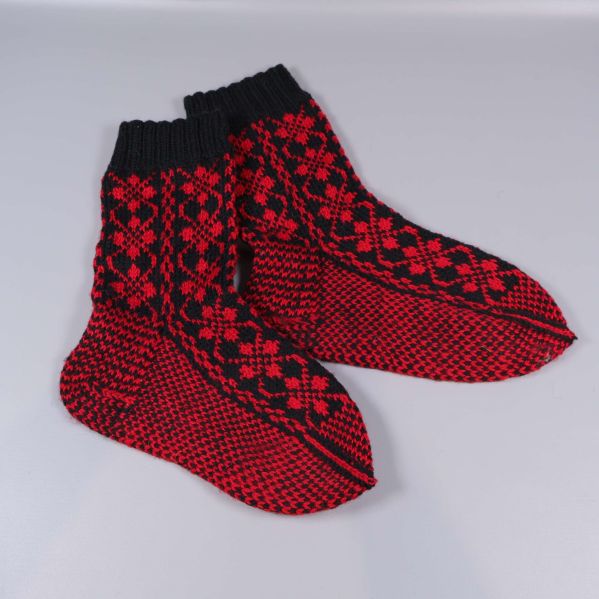 Stickade strumpor med svart kant och röd botten, liggande platt