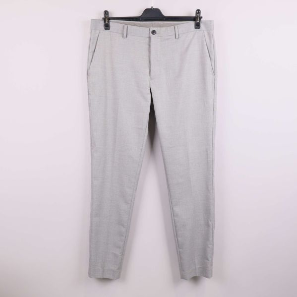 Slim fit ljusgrå kostymbyxa hänger mot vit vägg