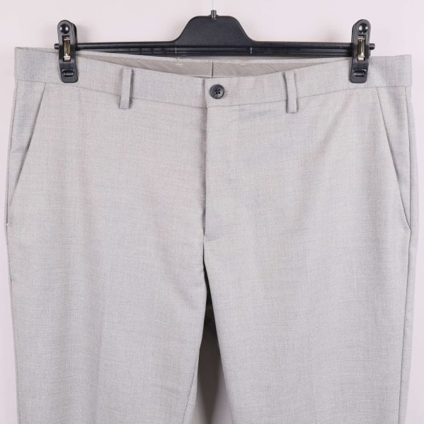 Närbild av framfickor och midjeknapp på ljusgrå byxa