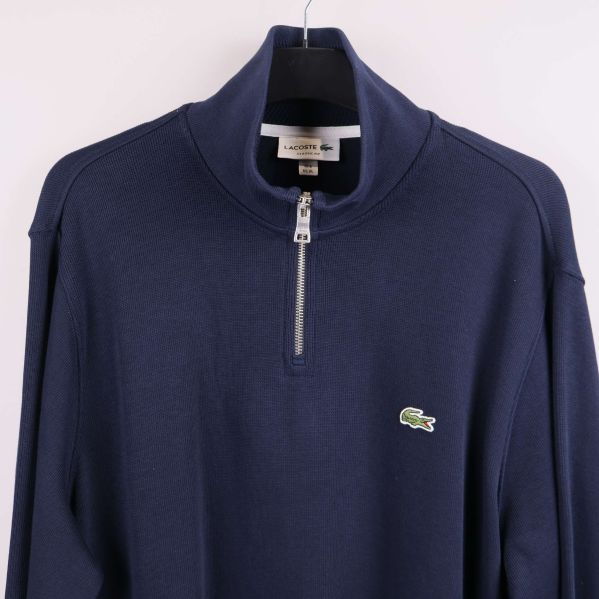 Närbild av tröjans bröstparti med halv dragkedja och broderad logga