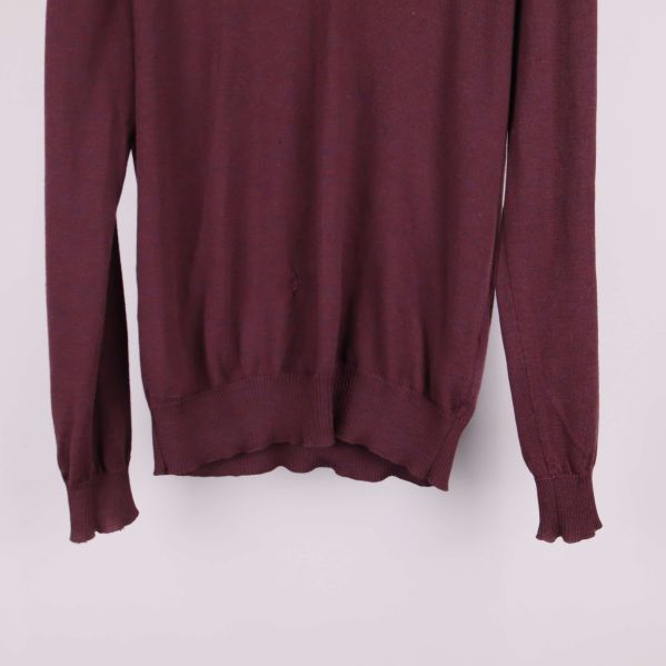 Nederkant och ärmslut på vinröd tröja i närbild