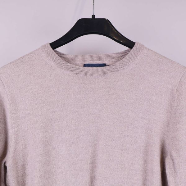 Närbild på halsringning och övre del av beige stickad tröja