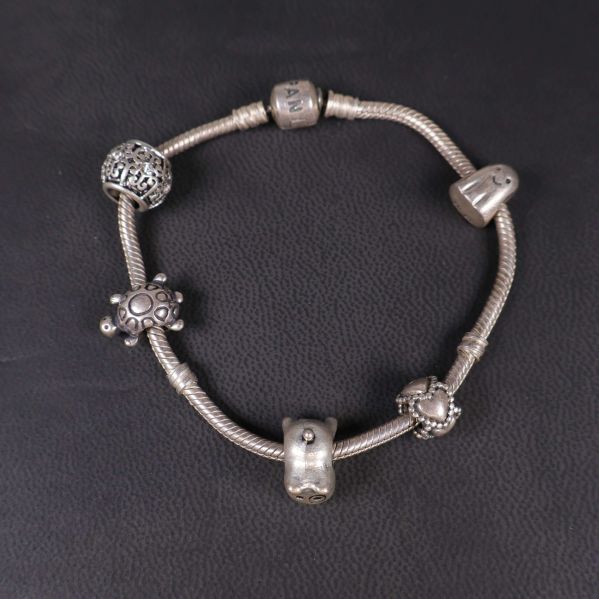 Silverfärgat armband med fem olika berlocker liggande på mörk yta