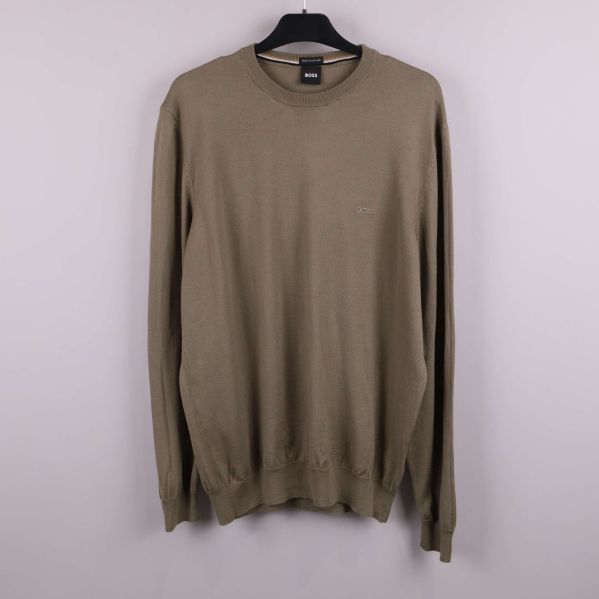 Beige stickad tröja på galge mot ljus bakgrund