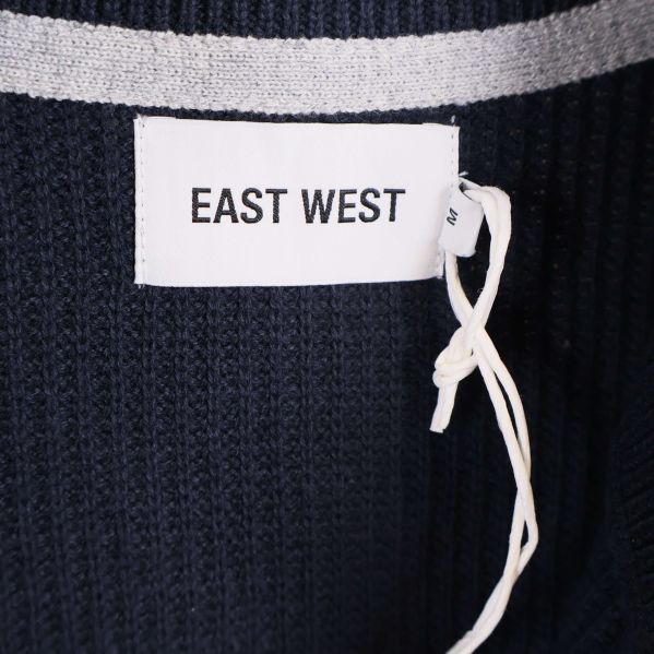 Närbild på vit etikett med texten EAST WEST i nacken