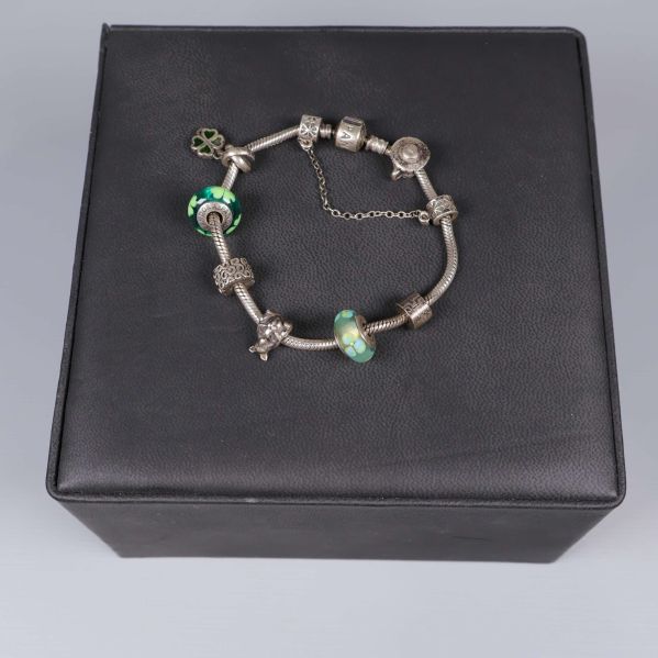 Armbandet visas cirkulärt med berlocker och gröna pärlor