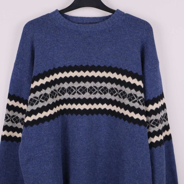 Närbild på bröstparti med svartvitt mönster på blå stickad tröja