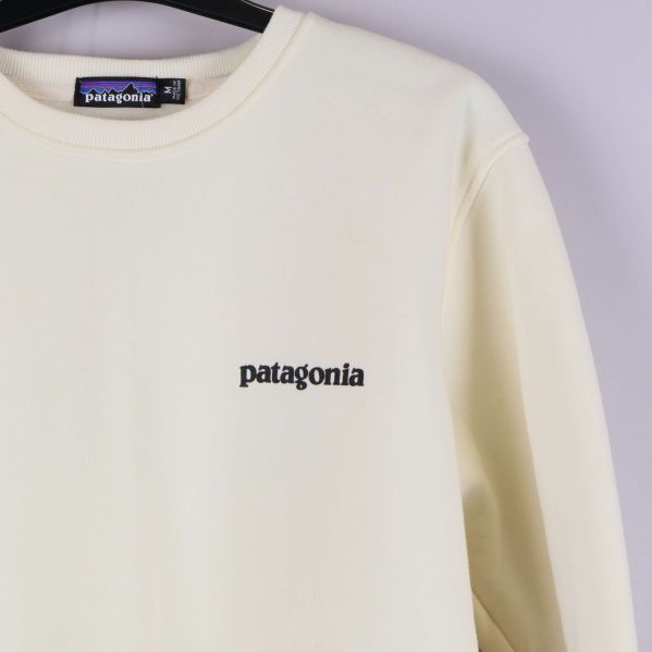 Närbild av främre loggan på krämvit sweatshirt