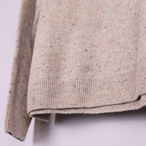 Nedre kant av beige stickad tröja med färgstänk