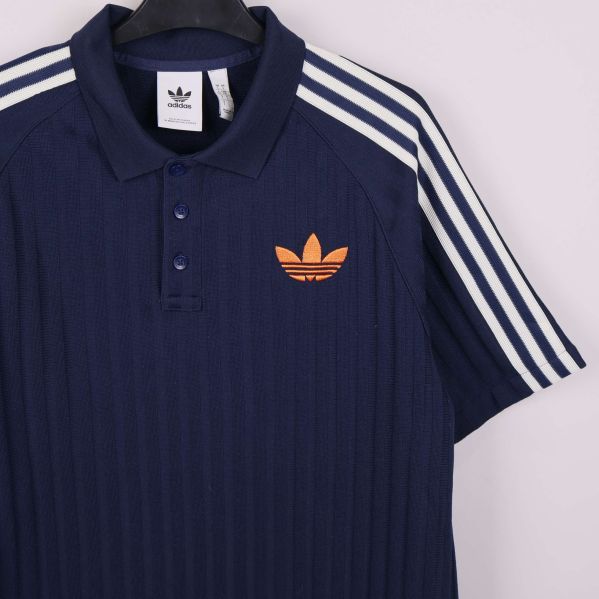 Närbild på piké med orange adidasmärke och vita axelränder