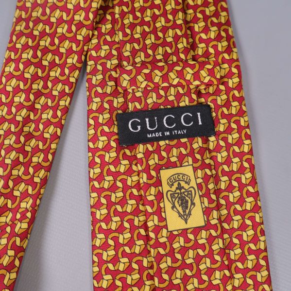 Närbild på Gucci etikett och gul logga på slipsens baksida