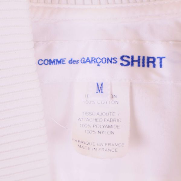 Närbild på märkesetikett med Comme des Garçons Shirt och storlek M