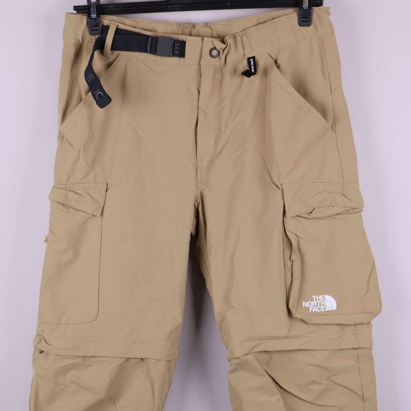 Detaljvy av fickor, bälte och logotyp på beige byxa