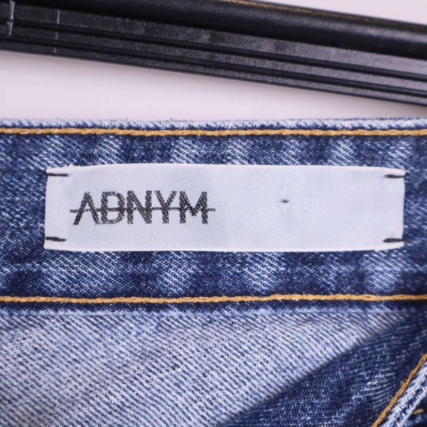 Närbild på vit etikett med tryckt logotyp adnym på jeansens insida