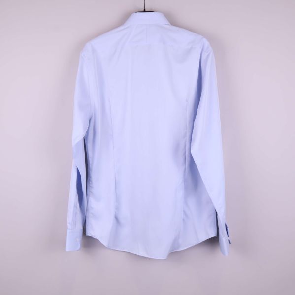 Baksidan av ljusblå skjorta visas mot ljus bakgrund