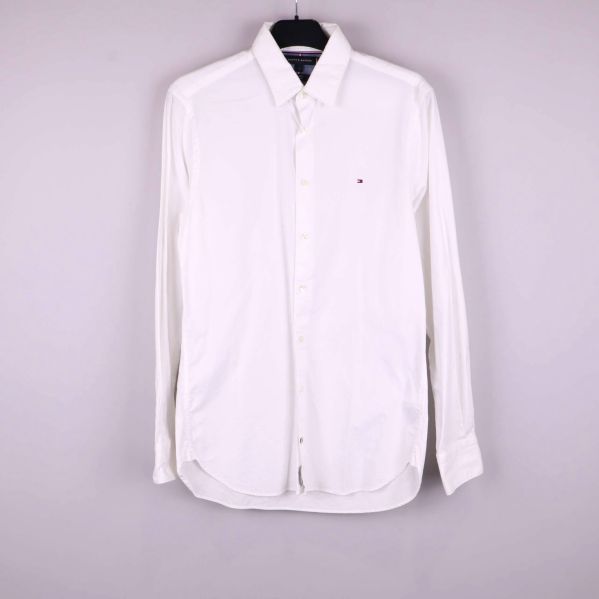 Vit långärmad skjorta på galge mot ljus bakgrund