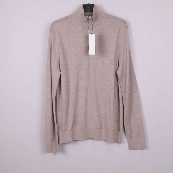 Beige tröja med halvzip upphängd mot ljus bakgrund
