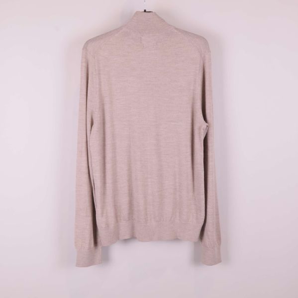 Beige stickad tröja sedd bakifrån på galge