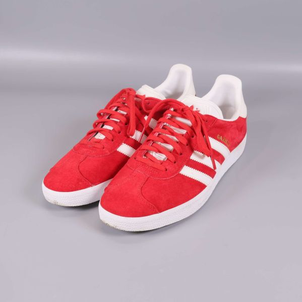 Röda sneakers med vita ränder och sula, sedd framifrån