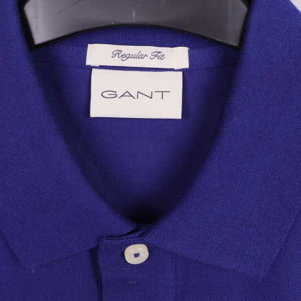 Närbild på GANT-logotyp och krage av blå pikétröja