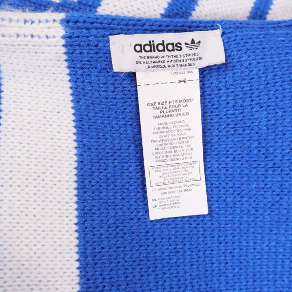 Närbild på tvättrådslapp med adidaslogga på blåvit stickad halsduk