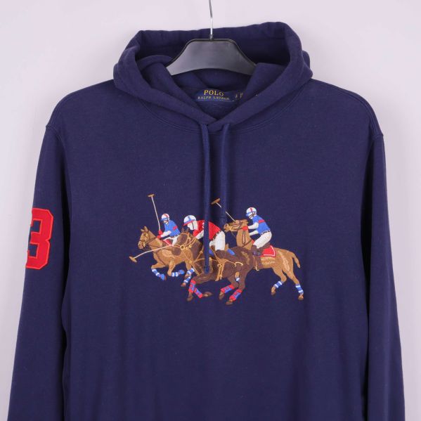 Närbild på broderat polospelmotiv och röd siffra på ärmen