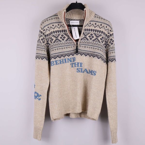 Framsidan av beige stickad tröja med blå mönster och text