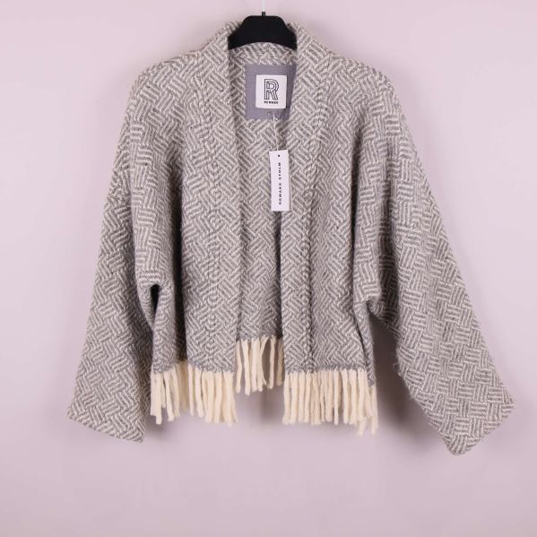 Kort jacka med mönster och fransar framtill hänger på galge