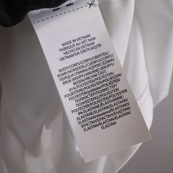 Materialetikett på vit pikétröja visar polyester och elastan