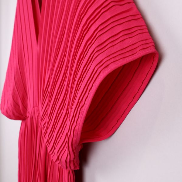 Närbild på cerise klänning med plisserade detaljer