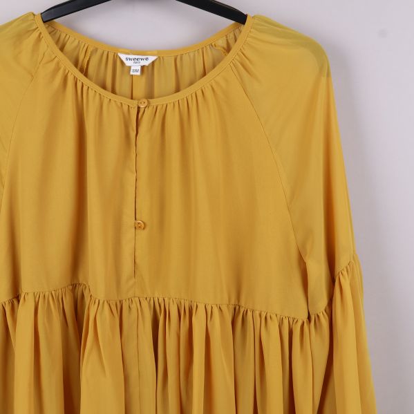Närbild på framsida av gul blus med knapp