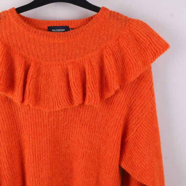 Närbild på orange volangtröja i hålstickad design