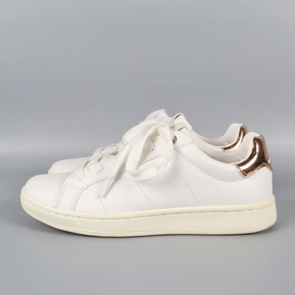 Sida av sneakers med kopparfärgade detaljer