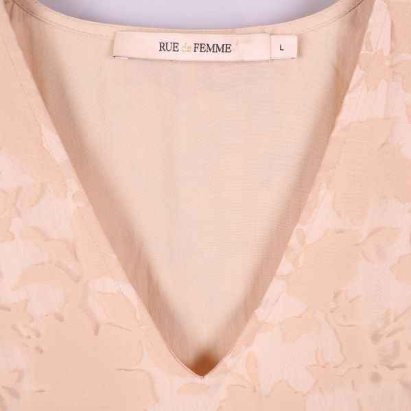 Närbild på v-ringning och varumärkestag i beige blommig klänning