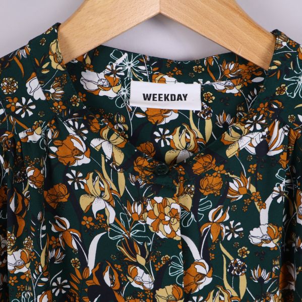 Närbild på Weekday-logotyp och blommigt tyg kring halsringningen