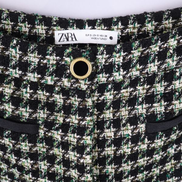 Närbild på hundtandsmönster och midjedetaljer med guldknapp