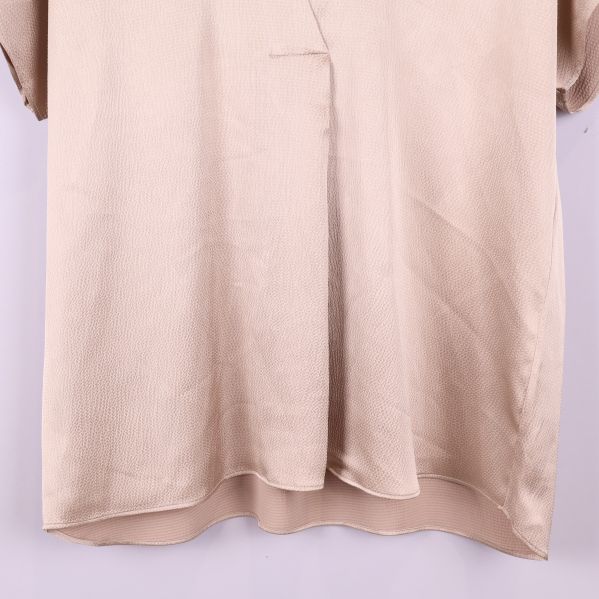 Nedre delen av blusens framsida i beige tyg
