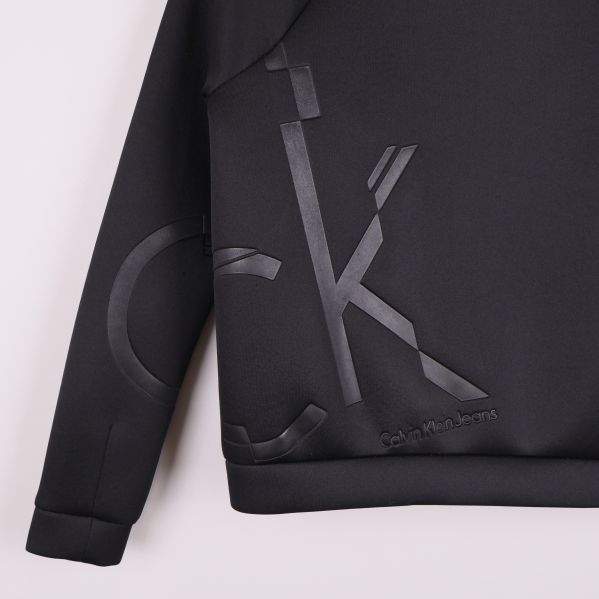 Närbild på blank CK-logga på svart jacka